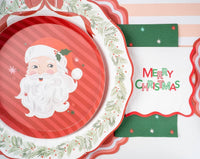Place setting with the Santa dessert plate on a green wreath-rim plate, a Merry Christmas banner, and a gold fork.