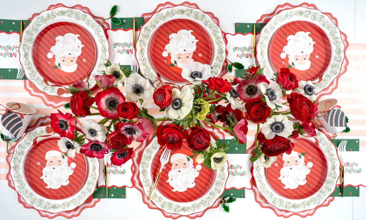 Overhead of Santa-plate settings on wreath dinner plates with red anemones, green place cards, and a striped runner.