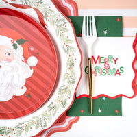 Place setting with a Santa plate, a white scalloped plate, the green star guest towel, and a green Merry Christmas banner.