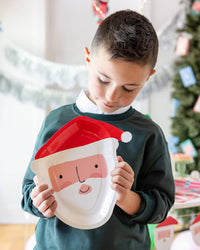 Child holding up a Santa-shaped paper plate at a holiday setting