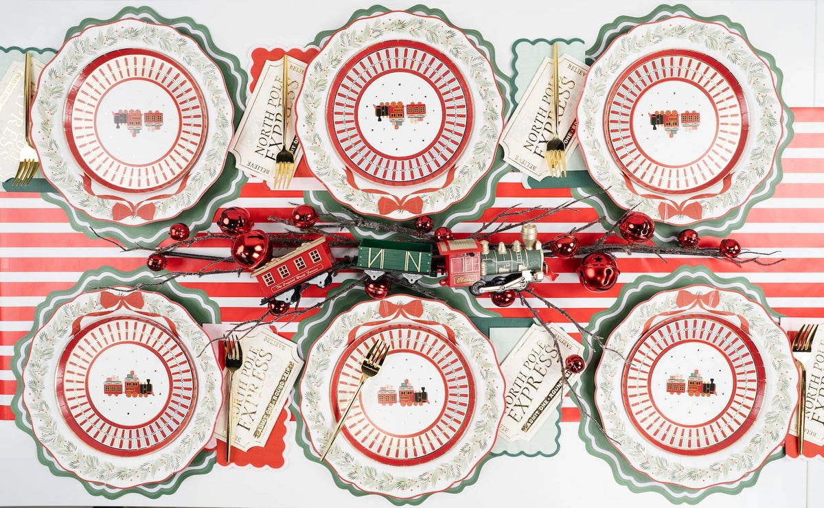 Overhead of Santa and wreath plate settings with a striped runner, red ornaments, and gold cutlery.