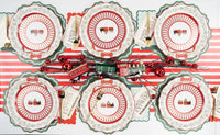 Overhead of Santa and wreath plate settings with a striped runner, red ornaments, and gold cutlery.