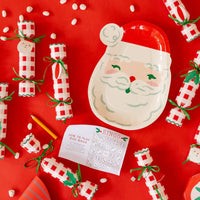 Flat lay of party supplies showing a Santa plate surrounded by Christmas party plates, Christmas crackers, and the dice bingo game.