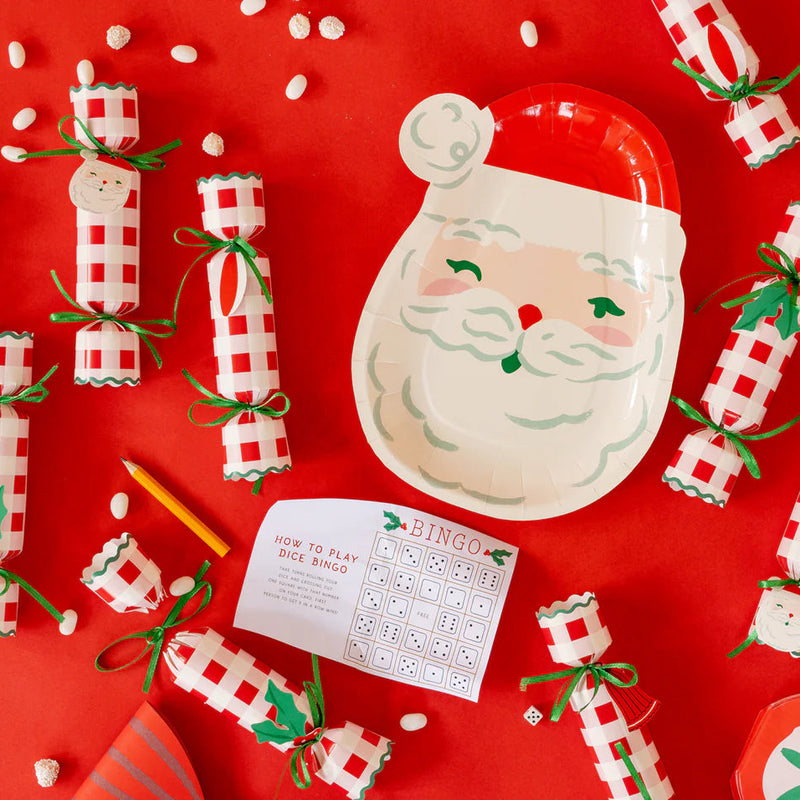 Flat lay of party supplies showing a Santa plate surrounded by Christmas party plates, Christmas crackers, and the dice bingo game.