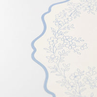 close up of scalloped edge on blue botanical paper placemat.
