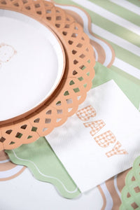 Close up angled view of the scalloped basketweave paper plate acting as a charger underneath a white dinner plate.