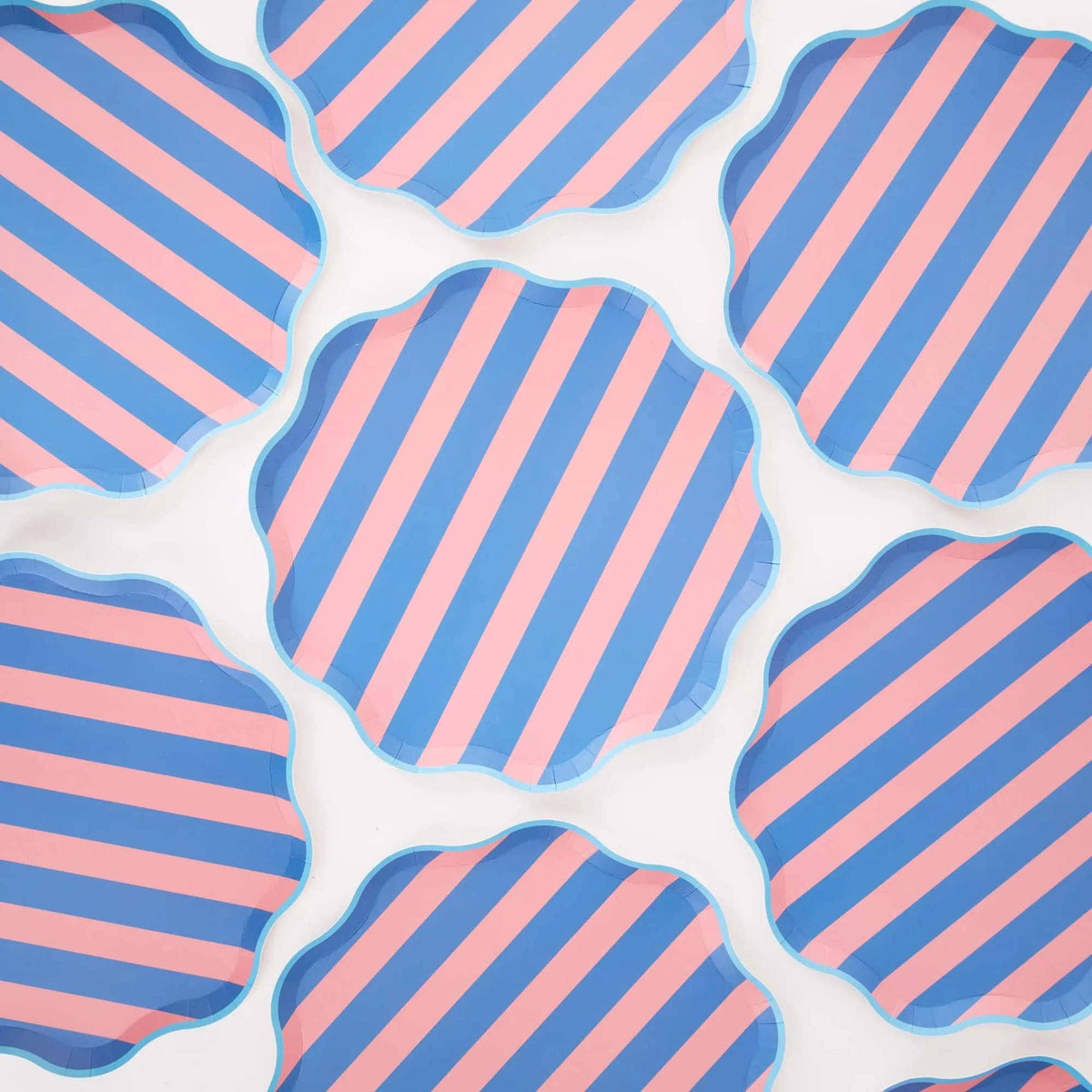 Multiple pink and blue cabana stripe scalloped paper plates arranged in a repeating pattern on a white background.