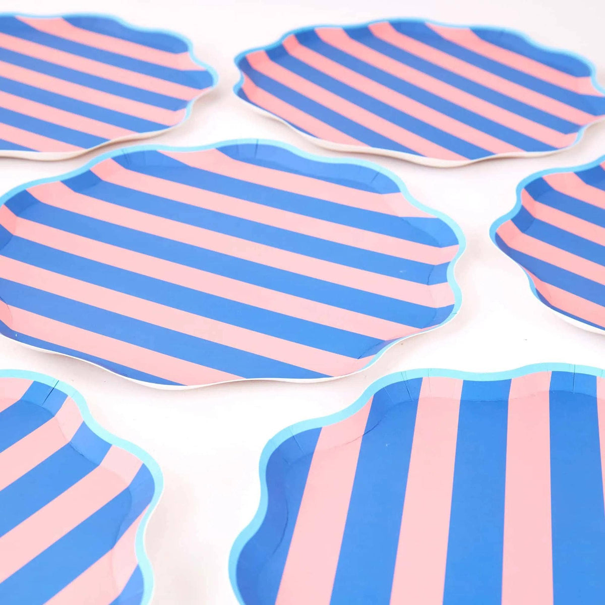 Group of pink and blue cabana stripe scalloped plates stacked and fanned on a white surface.