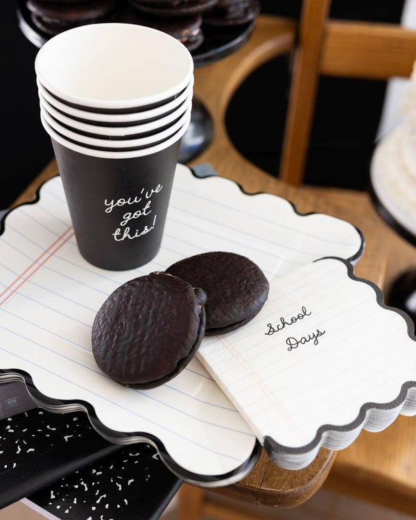 Styled back to school dessert table with School Days notebook paper napkins on a notebook scalloped plate next to a black "you've got this" paper party cup and chocolate whoopie pies