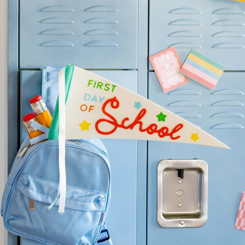 School pennant displayed on backpack in front of lockers.