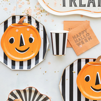 Halloween tableware flat lay with black-and-white striped plates, pumpkin plates, striped cups, and orange cocktail napkins.