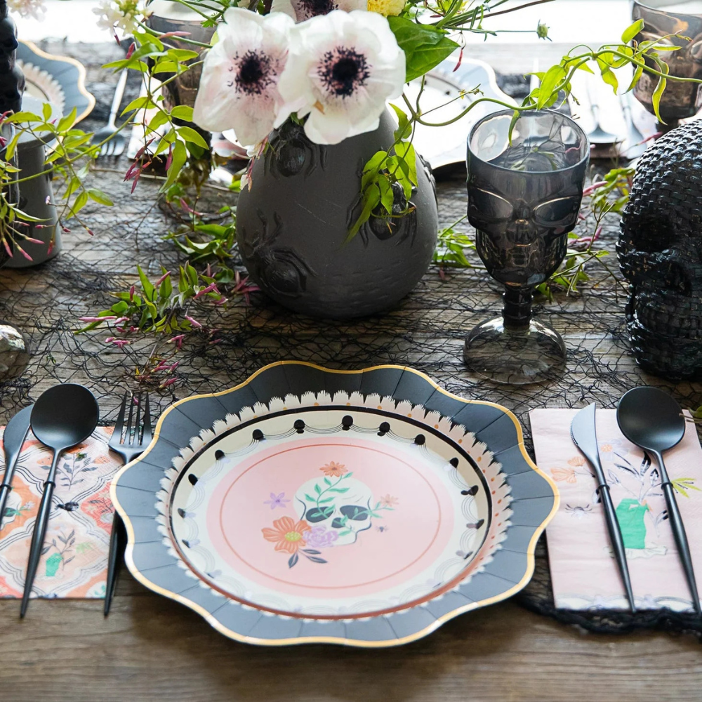 Halloween dinner party table setting with skull goblets, floral centerpiece, and guest towels placed under black flatware.