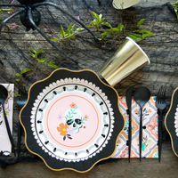 Close-up of Halloween place setting with floral skull dinner napkin, scalloped black plate, and gold accents.
