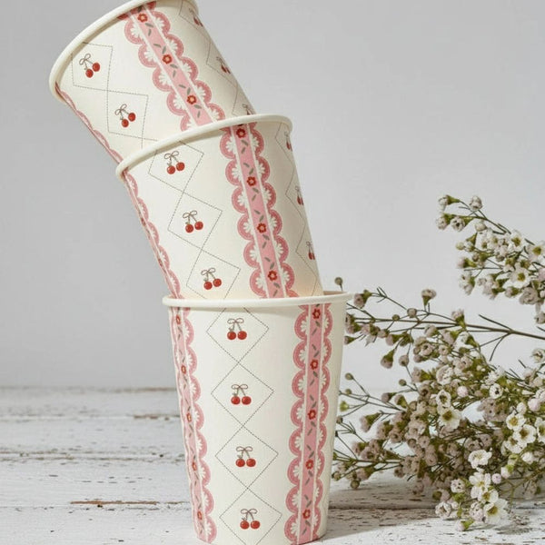 A stack of three cherry themed paper cups next to white wildflowers