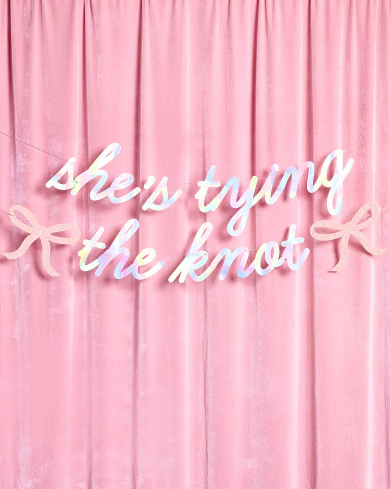 She's Tying the Knot iridescent banner hung on pink velvet backdrop for bridal shower