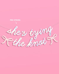Full She's Tying the Knot iridescent foil banner with pink glitter bows pre-strung on silver cords on pink background