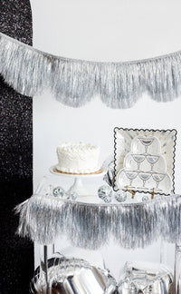 Silver fringe banner hung as a backdrop above a styled cake table