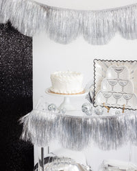 Silver fringe banner styled as a backdrop behind a cake and dessert table