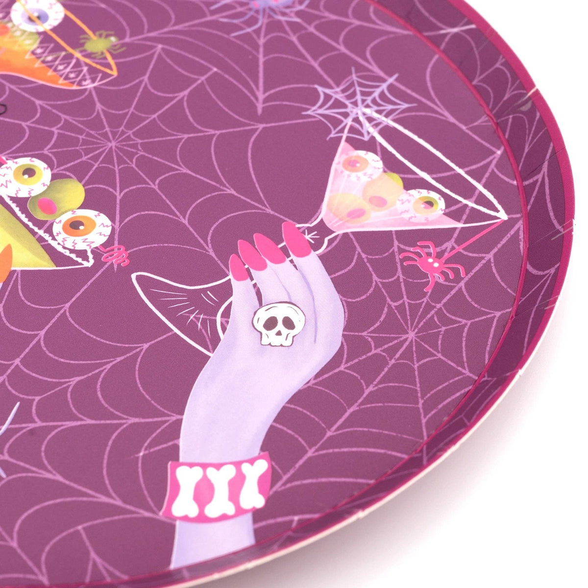 Macro detail shot of the paper plate featuring a manicured hand with a skull ring holding a round cocktail glass.