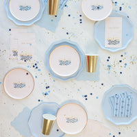 Tablescape of sky blue plates with gold cups and confetti—pastel blue paper plates for celebrations.