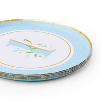 Angled stack of sky blue first birthday paper plates with floral illustrated number 1 and gold foil rim on white background