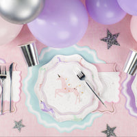 Close shot: pink and lavender balloon cluster above plate stack and rainbow napkin.
