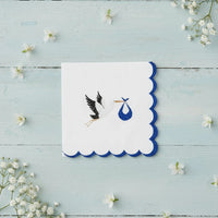 Blue stork napkin centered on a light wood surface with white wildflowers