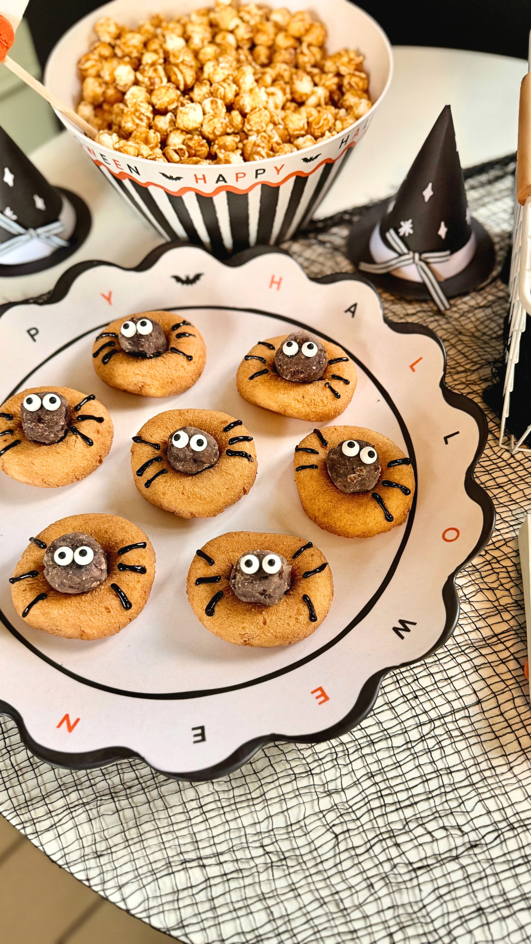 Scalloped white Happy Halloween platter with a black rim and orange and black lettering, served with spider cookies and caramel popcorn