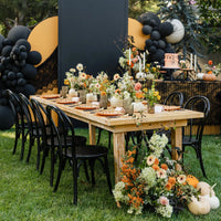 Outdoor Halloween dinner party table with orange spiderweb place settings, fall florals, white pumpkins, and black balloon garlands