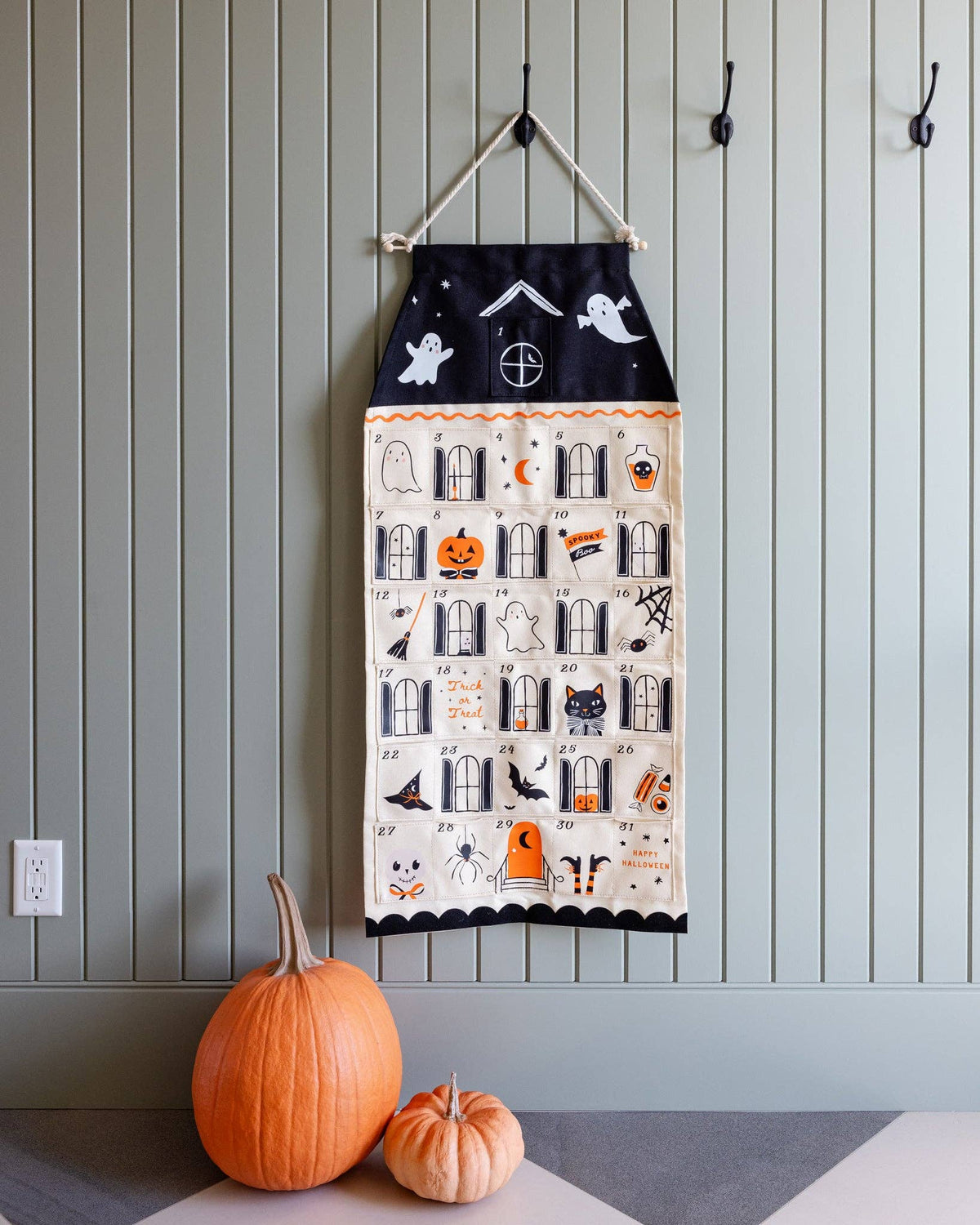 Canvas Halloween advent calendar hanging on a green beadboard wall above two orange pumpkins