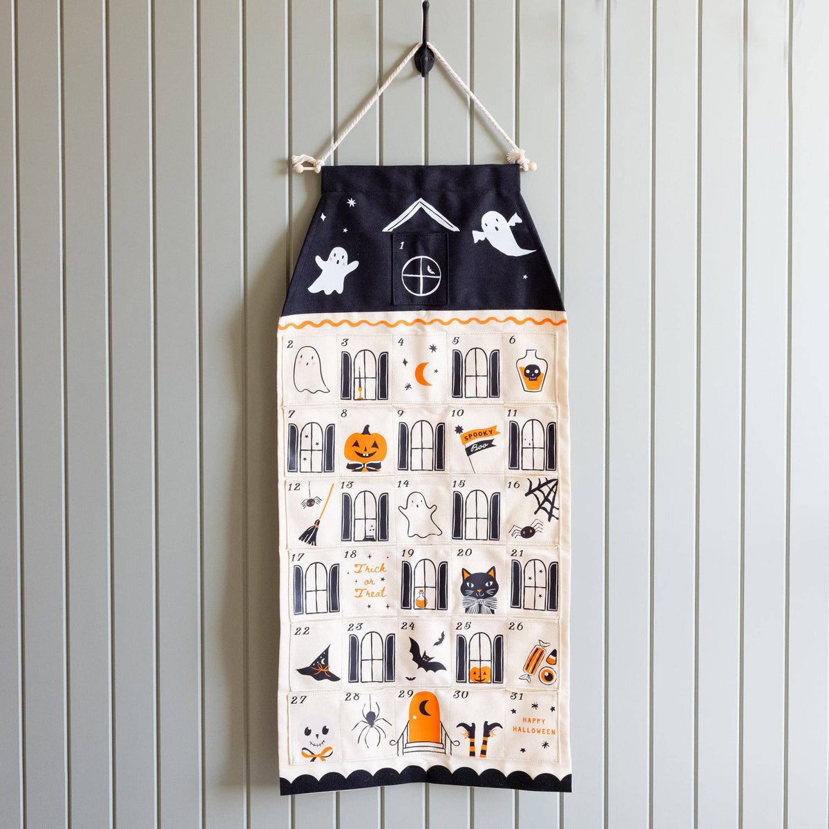 Halloween countdown calendar hung from a black hook on a beadboard wall, showing all 31 illustrated pockets