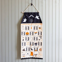 Halloween countdown calendar hung from a black hook on a beadboard wall, showing all 31 illustrated pockets