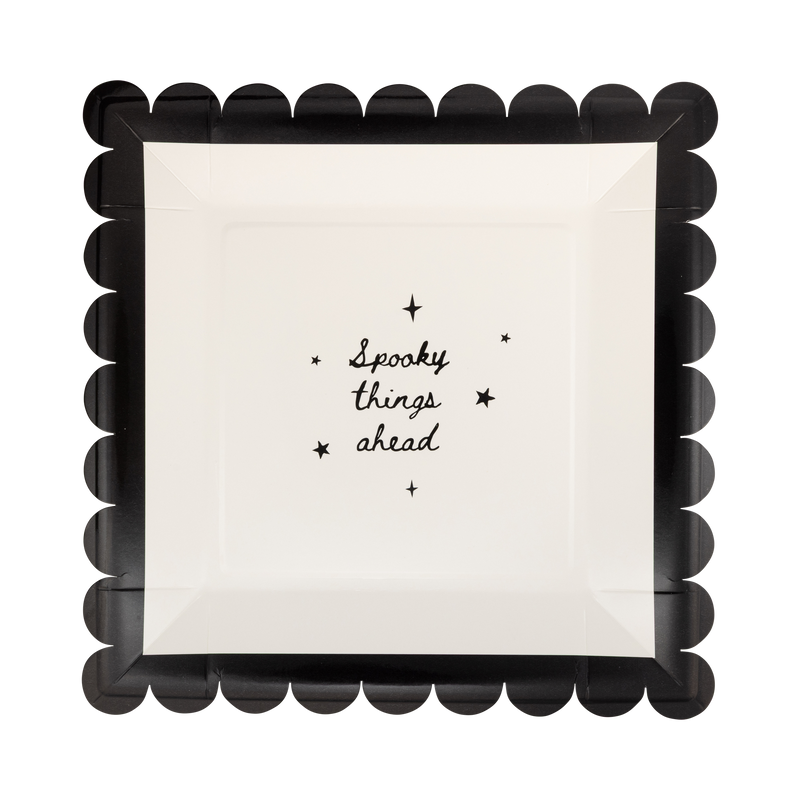 Cream scalloped paper plate with black "SPOOKY THINGS AHEAD" text and a black scalloped edge, front view.