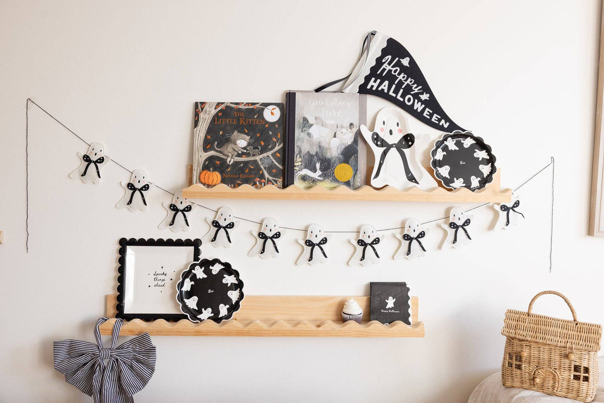 Decorative shelf with Halloween-themed items including Spooky things ahead paper plates, books, plates, and a banner on a white wall.