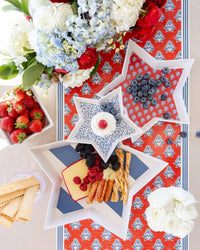 Three nesting star bamboo trays stacked with blueberries, cheese, breadsticks, and cupcake on red block print table runner