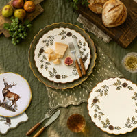 Overhead fall table with the stag plate, pinecone plates, cheese, bread, pears, and greenery on an olive cloth.