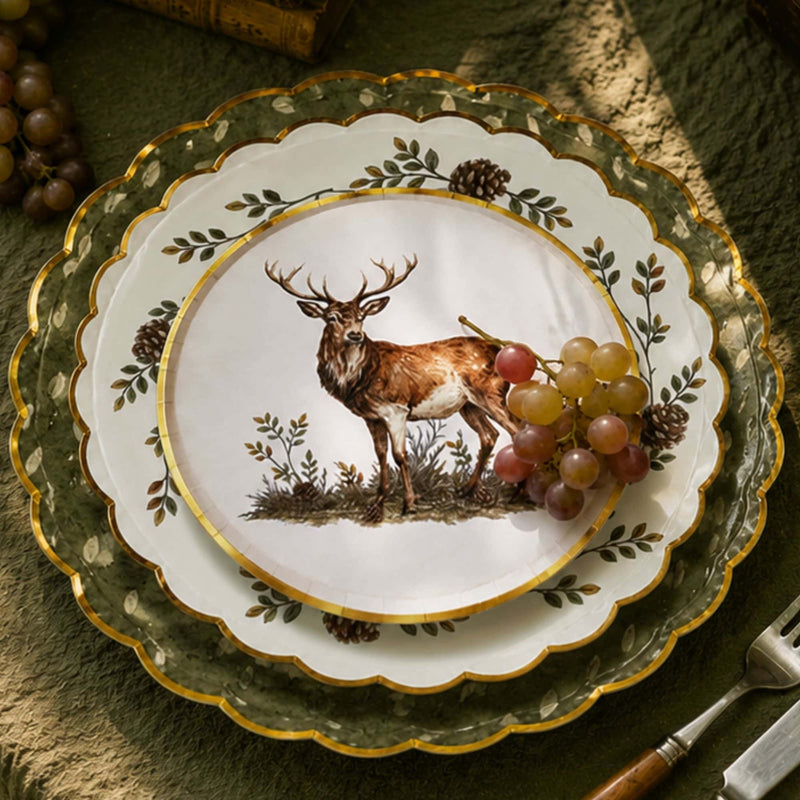 Place setting with the stag plate layered on a pinecone dessert plate and olive scalloped charger, grapes, and gold cutlery.
