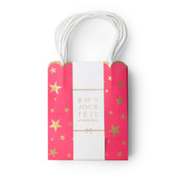 Pink gold-star favor bag wrapped in a white Bonjour Fête belly band, showing the scalloped top and paper handles.