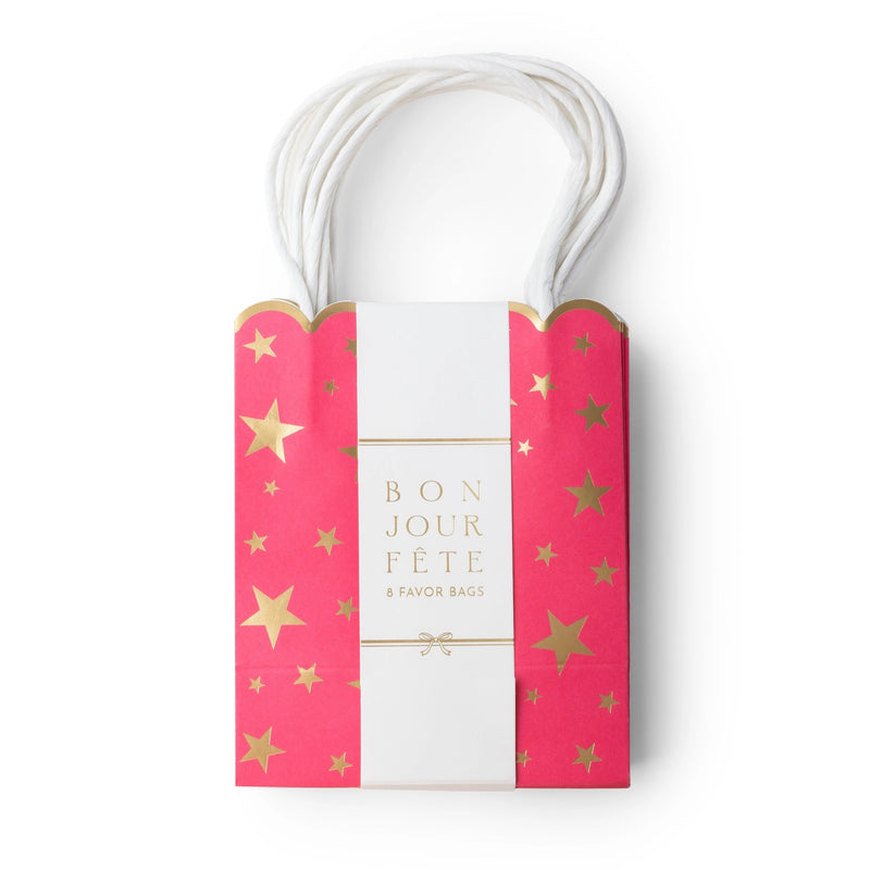 Pink gold-star favor bag wrapped in a white Bonjour Fête belly band, showing the scalloped top and paper handles.