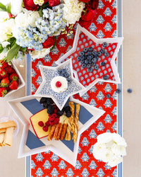 Overhead of star bamboo trays with cheese and berries on red block print floral paper table runner