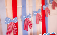 Close-up detail of stars and stripes paper bows on cream twine with blue star-print tops and red-striped tails against red and blue streamers