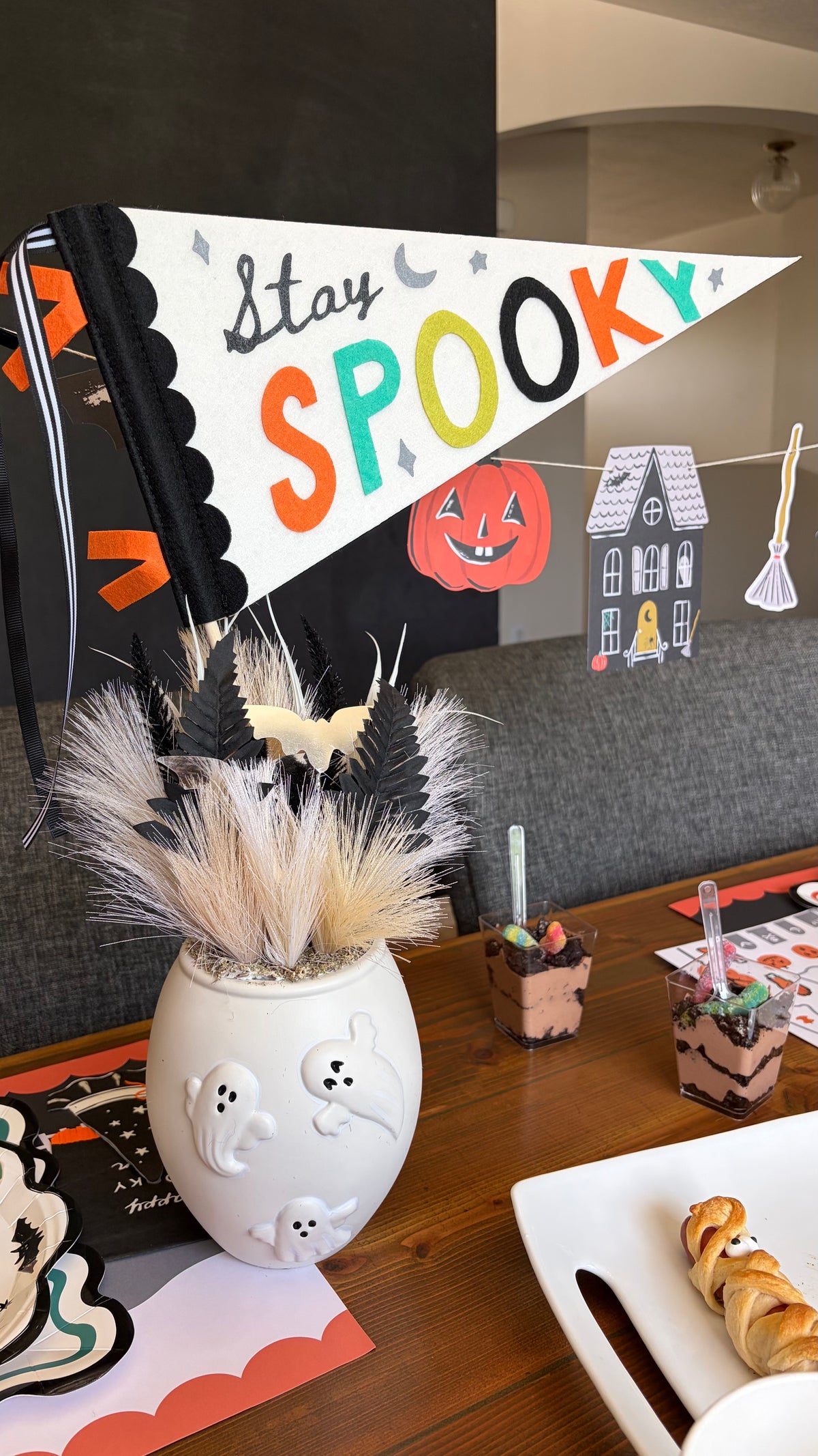 Stay Spooky felt pennant in a white vase with pampas grass on a Halloween table with icon plates and small bites