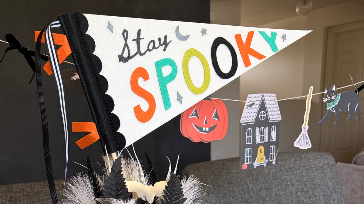 Stay Spooky felt pennant flag styled against a wall with a vintage Halloween character banner and paper lanterns in the background