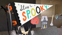 Stay Spooky felt pennant flag styled against a wall with a vintage Halloween character banner and paper lanterns in the background