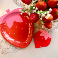 Strawberry shaped plate and matching strawberry napkin beside fresh strawberries bouquet.
