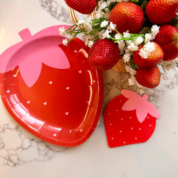 Strawberry shaped plate and matching strawberry napkin beside fresh strawberries bouquet.