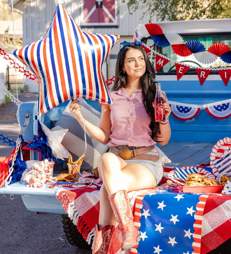Close-up of woman holding red white and blue striped star mylar balloon in decorated vintage truck bed with 4th of July party food and decor