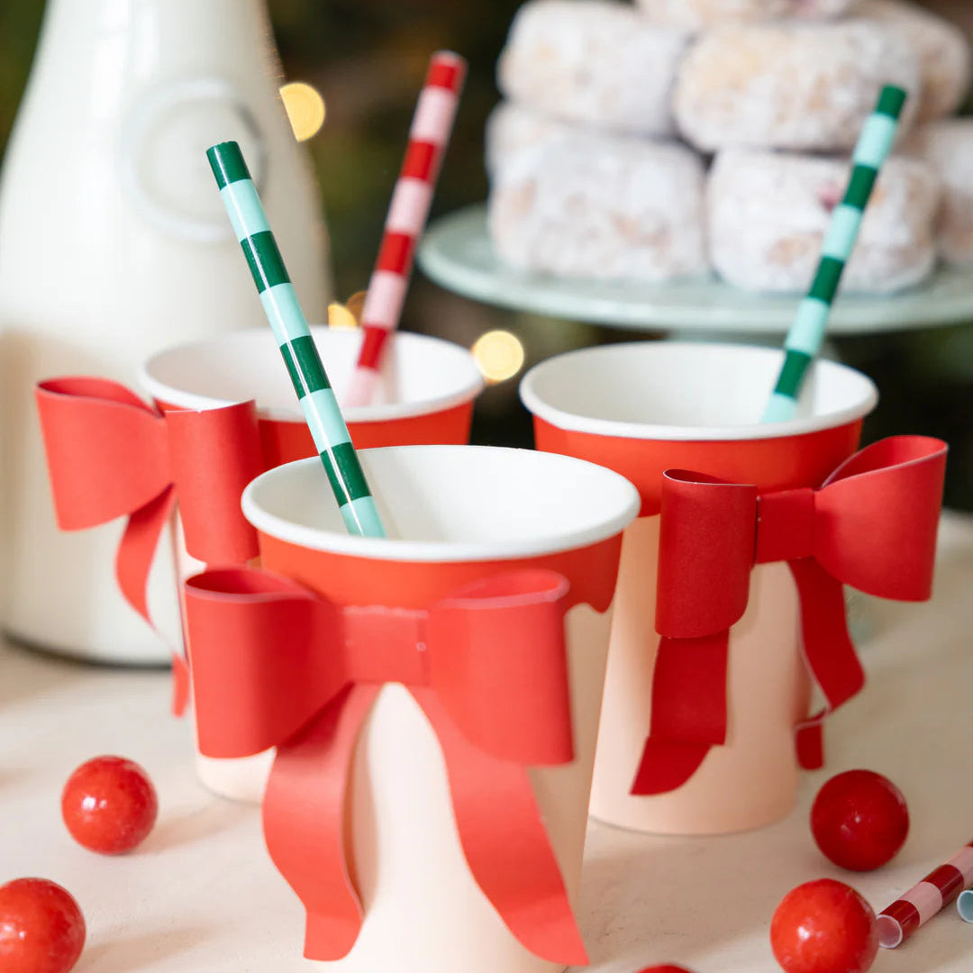 Styled setup of three Christmas paper cups with straws and donuts in the background, showing the bow cups in use.