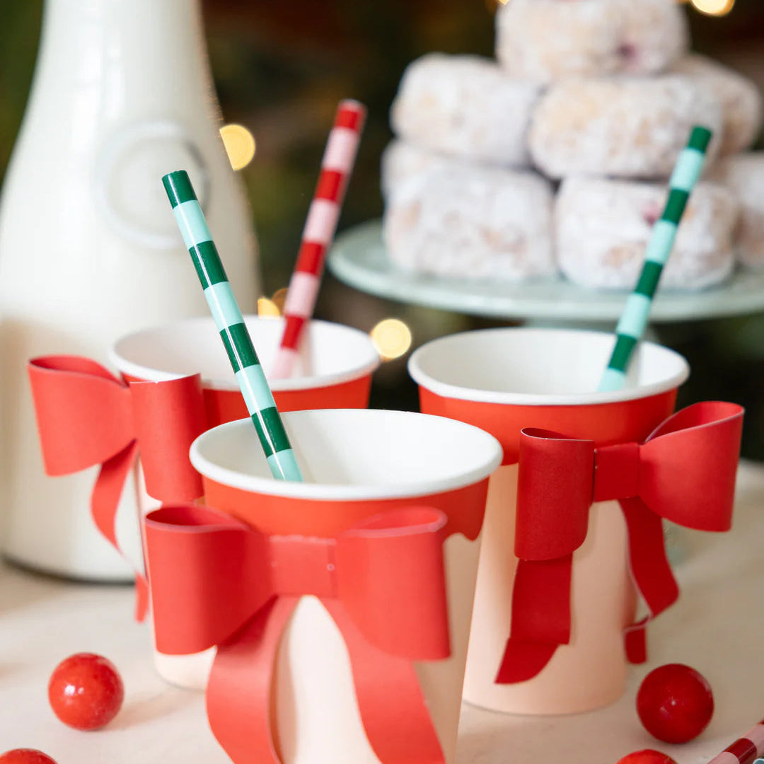 Close-up of Christmas straws and milk served in the matching bow cups, set against a background of donuts and string lights.