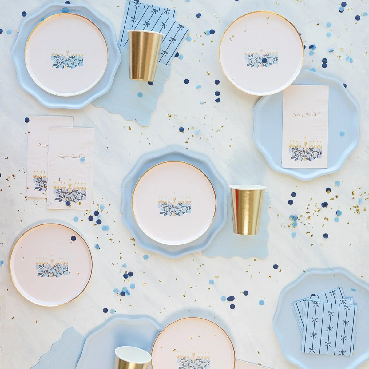Place setting featuring the hanukkah paper plates layered over a large blue scalloped charger with a white floral centerpiece.